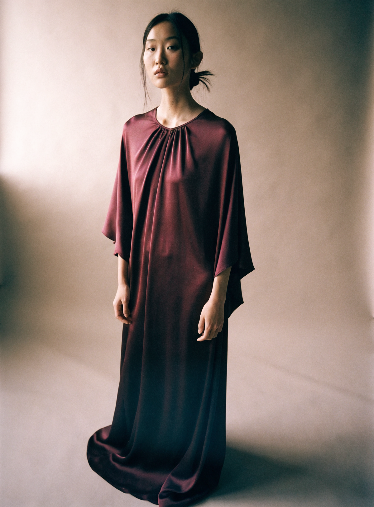Model in a floor-length burgundy dress against a warm neutral studio backdrop